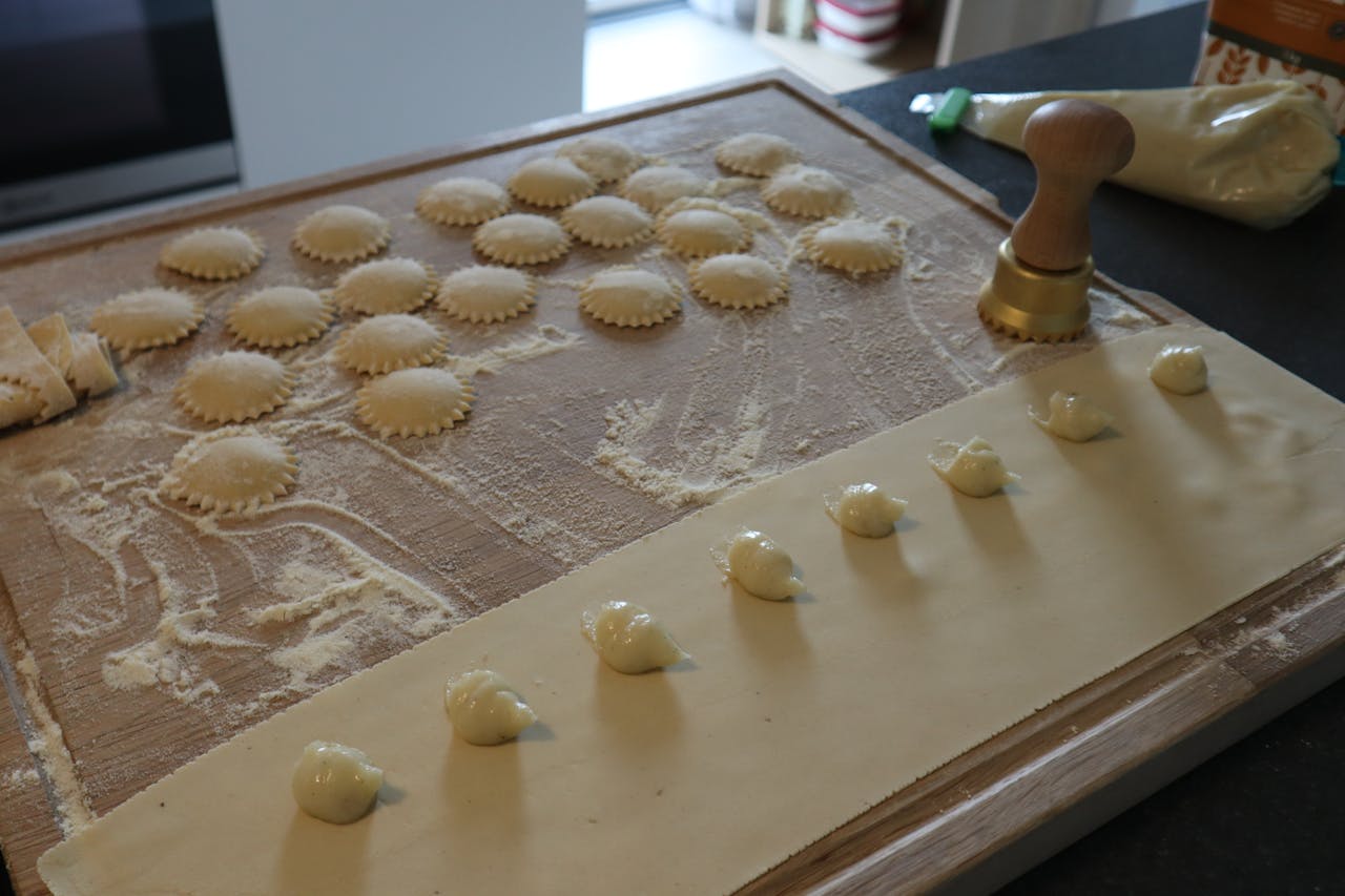 A close-up of fresh ravioli being prepared on a floured board with a pasta stamp nearby.