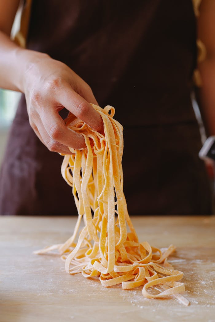 A close-up image showcasing a hand holding fresh uncooked pasta on a wooden surface.